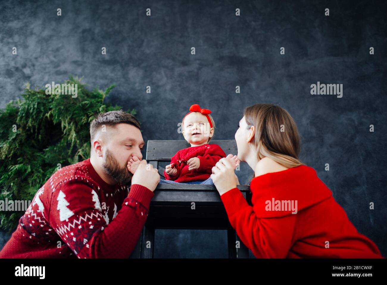 La famille en pull rouge embrasse les talons du bébé. Banque D'Images