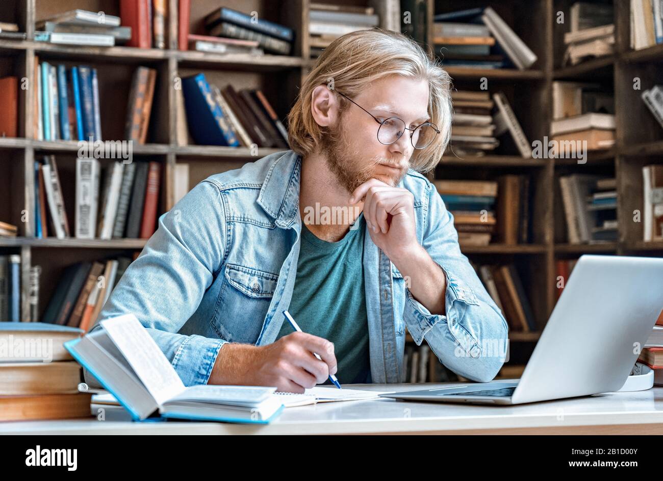 Bureau focalisé de la bibliothèque de jeune homme lire ordinateur portable moderne faire des notes e concept d'éducation Banque D'Images