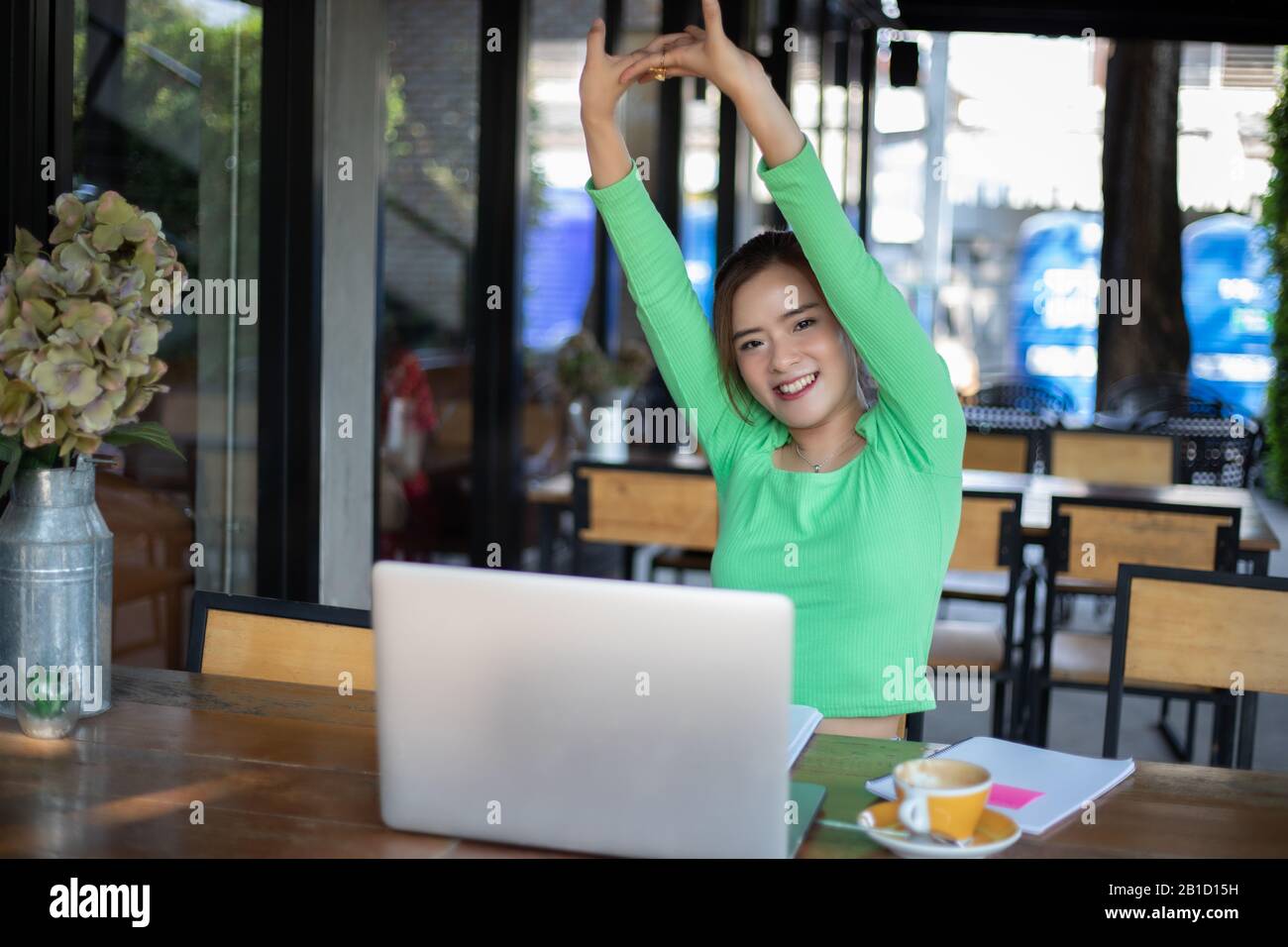 Une femme asiatique s'étirant après avoir lu le livre et travaillé dur et souriant dans un café Banque D'Images