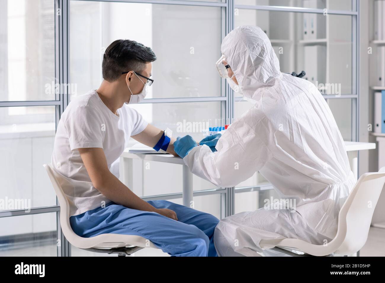 Spécialiste médical en cas de risque biologique, prenant le sang d'un patient asiatique infecté mortel dans la zone de contrôle Banque D'Images