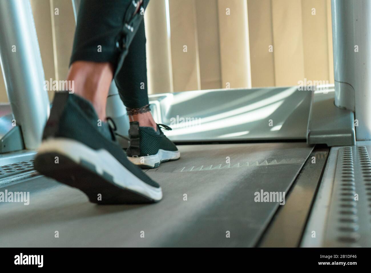 Gros plan sur les jambes de la femme pendant que vous courez sur le tapis roulant dans la salle de sport ensoleillée. Banque D'Images