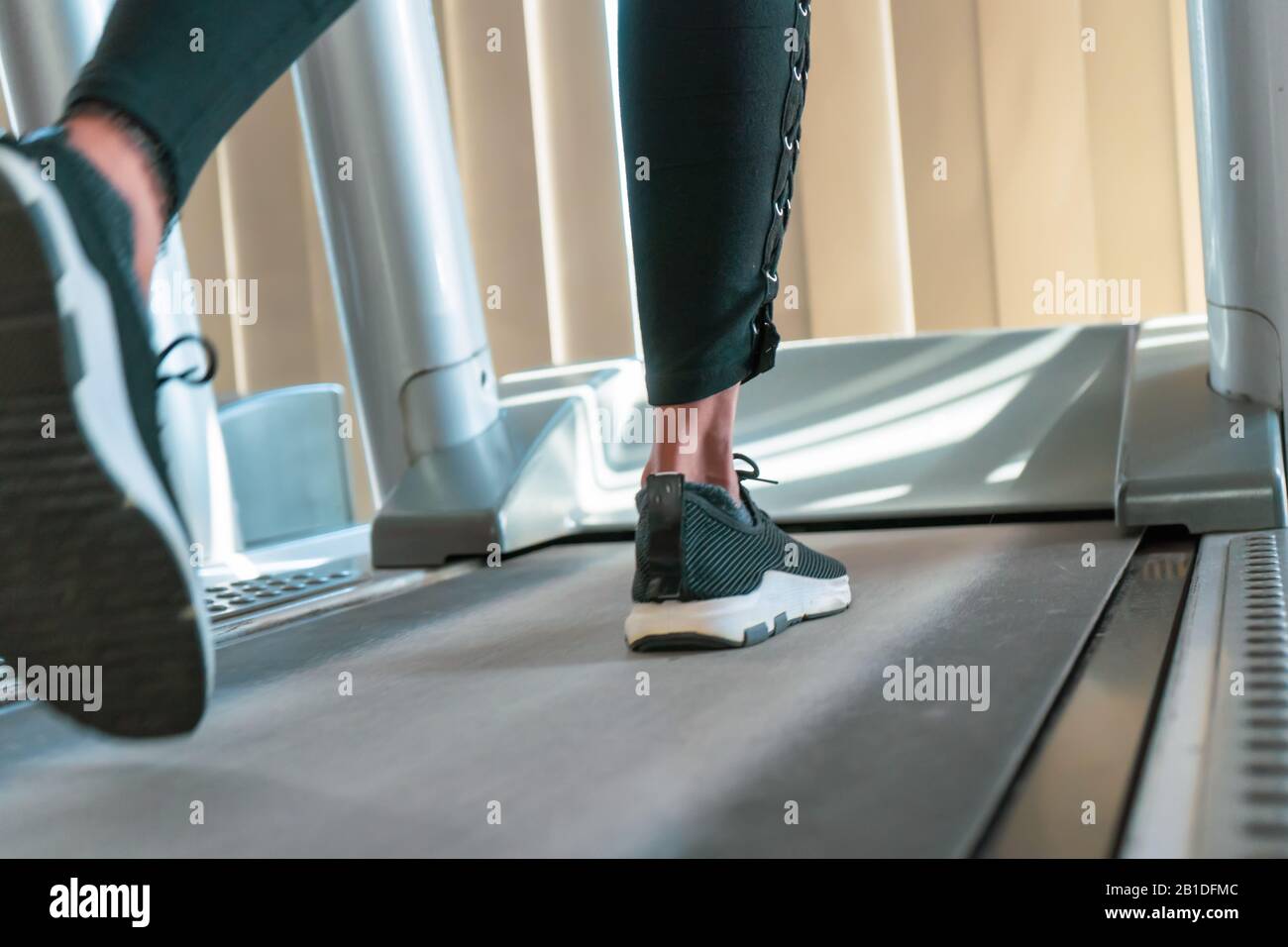 Gros plan sur les jambes de la femme pendant que vous courez sur le tapis roulant dans la salle de sport ensoleillée. Banque D'Images