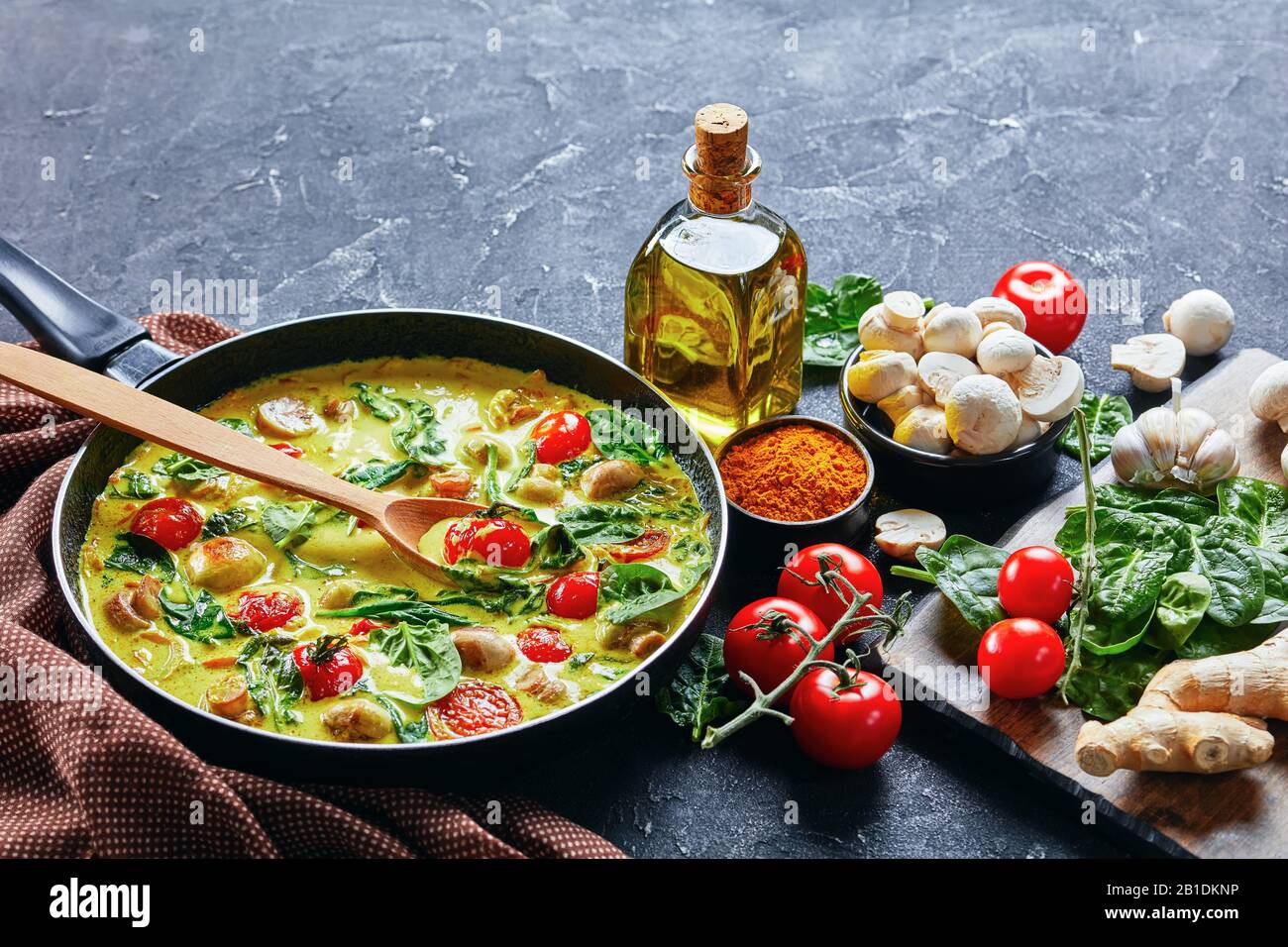 Curry de champignons à faible teneur en gras sur poêle à frire de lait de coco avec champagnes et légumes : épinards frais et tomates cerises sur fond de béton foncé Banque D'Images