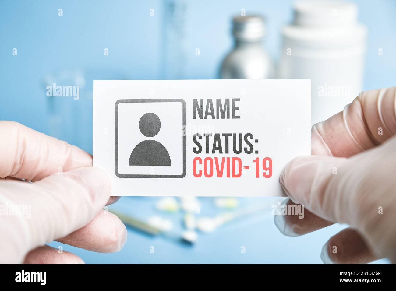Un médecin en gants possède une carte blanche avec les données personnelles d'une personne et son statut de membre infecté COVID-19 dans un contexte médical Banque D'Images