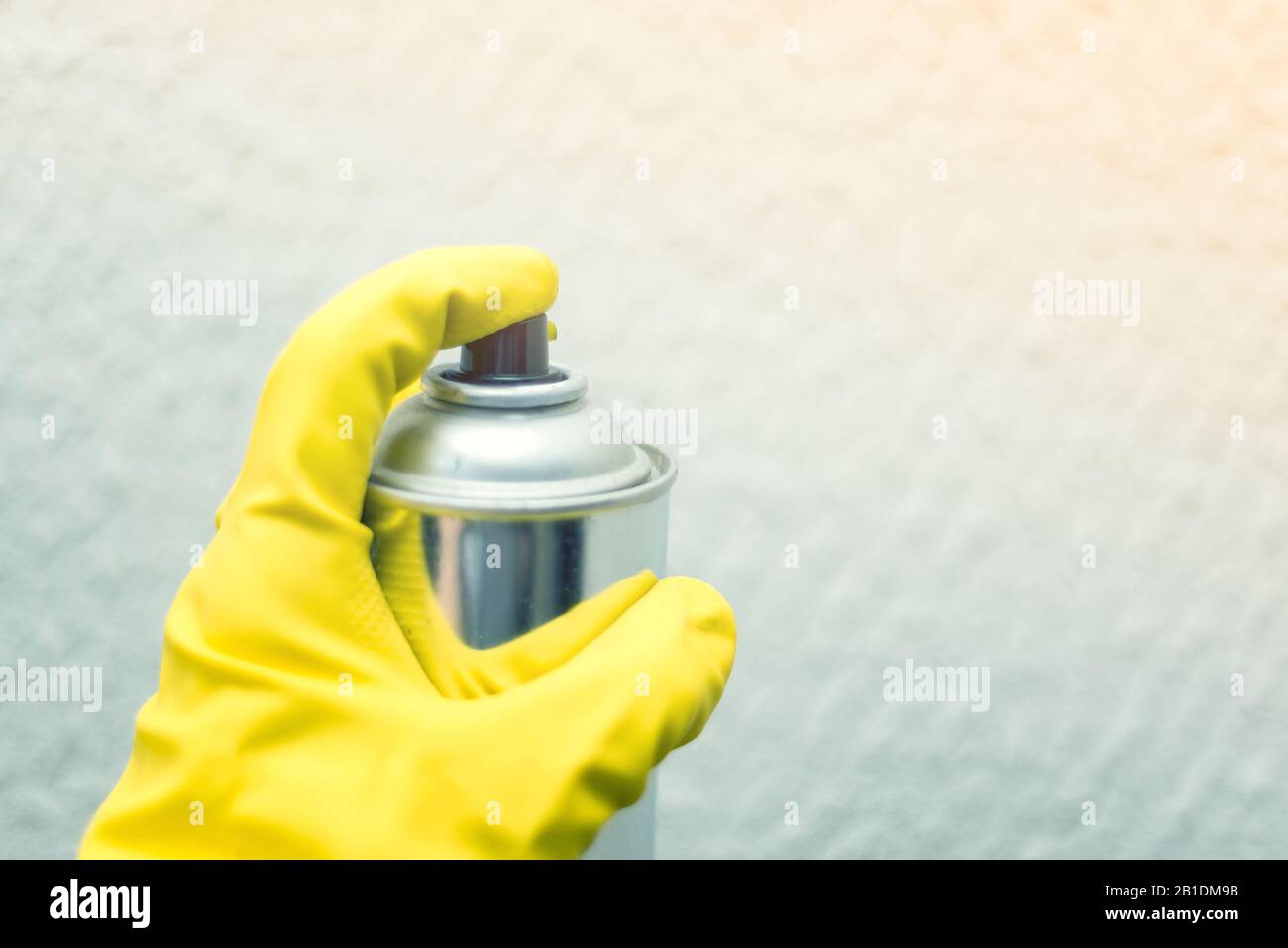 peinture des murs de la pulvérisation. main dans des gants en caoutchouc jaune tenant la peinture de pulvérisation. réparations Banque D'Images