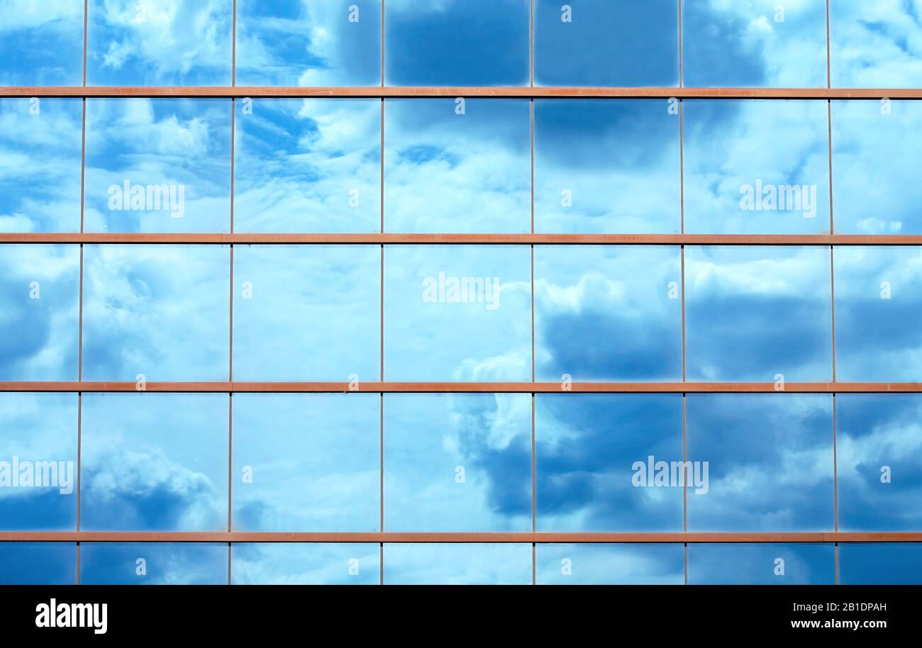 Beau ciel bleu et nuages reflétés sur de grands panneaux de glace de miroir de la fenêtre du bâtiment Banque D'Images