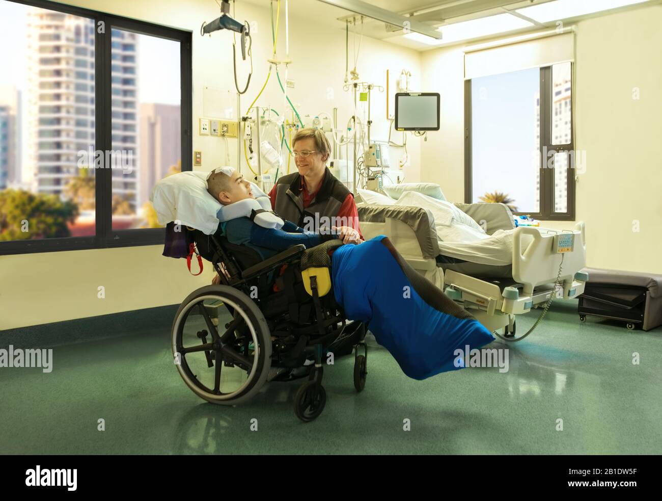 Père assis avec un fils handicapé en fauteuil roulant dans la salle d'hôpital après une chirurgie cérébrale, la tête couverte de bandage Banque D'Images
