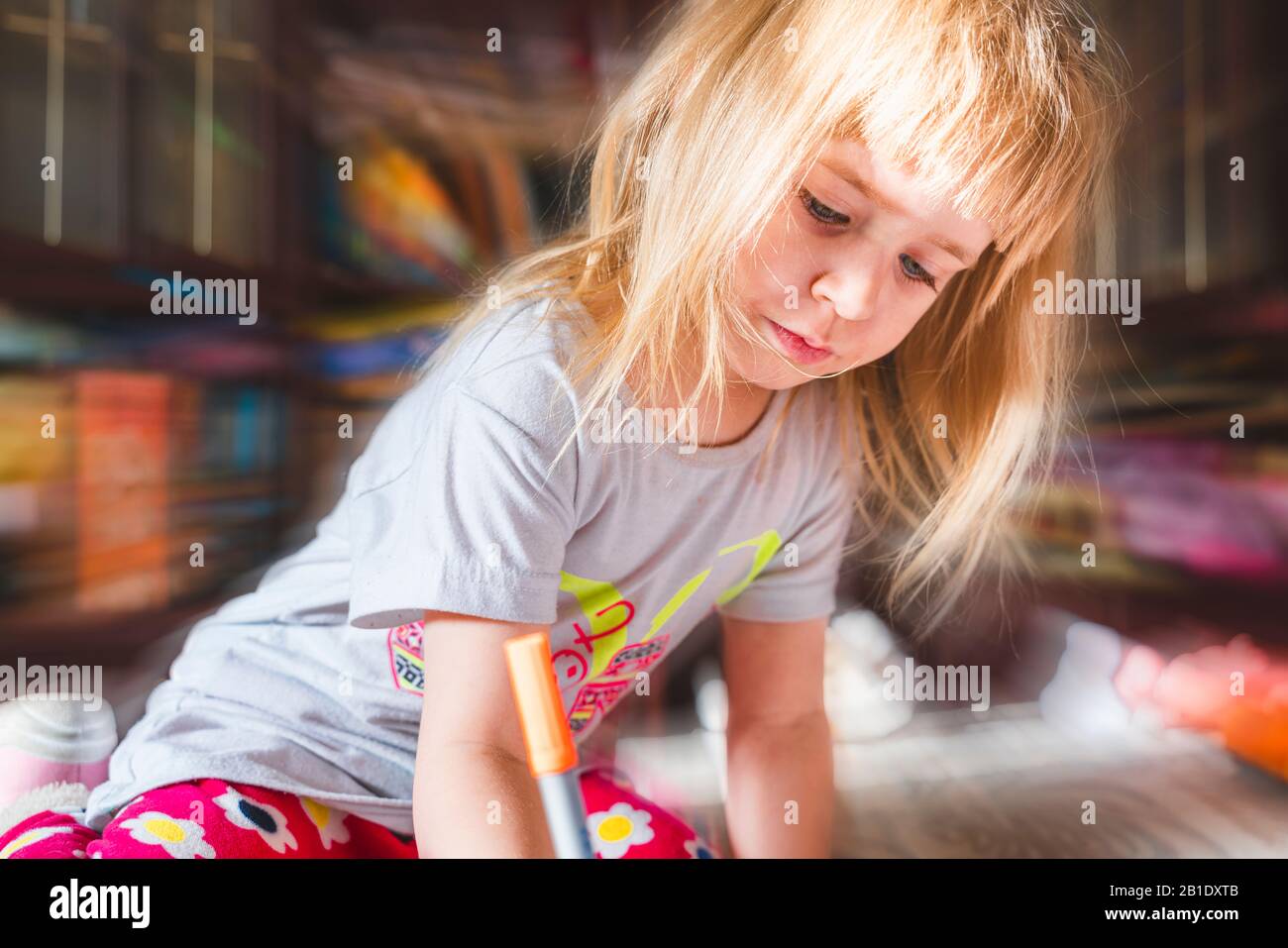 Jolie petite fille avec un dessin de cheveux blond à la maison. Image couleur Candid, gros plan. Concept d'évolution de l'enfant. Banque D'Images