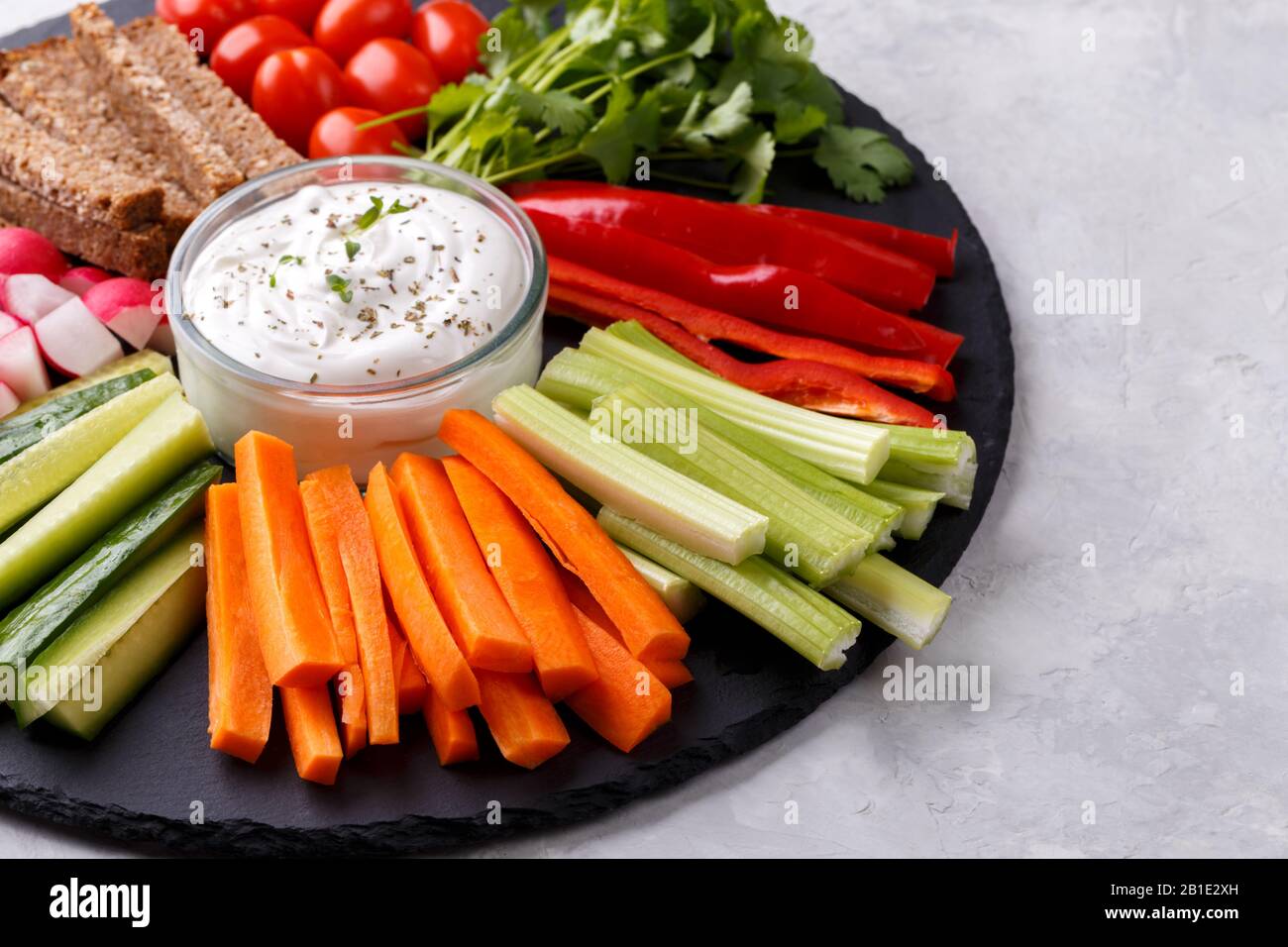 En-cas de légumes sains avec sauce au yaourt sur une planche ronde en pierre d'ardoise, vue de dessus rapprochée, espace de copie Banque D'Images