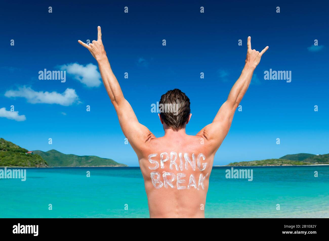 Dude avec Spring Break écrit dans la crème solaire sur son dos se balançant avec ses mains dans l'air sur une plage tropicale Banque D'Images