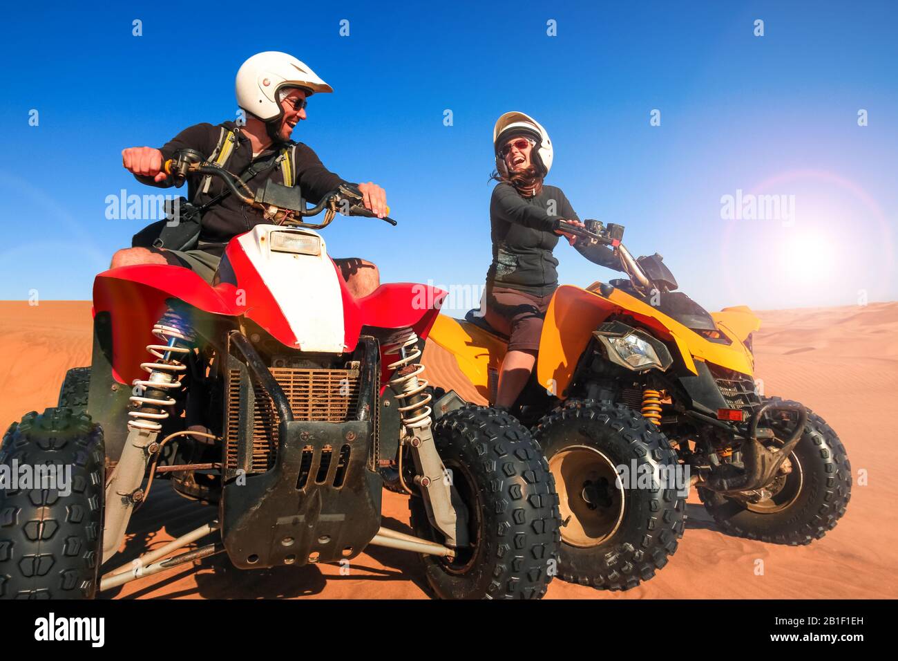 Quad Driving People - heureux souriant couple des cyclistes dans le sable désert coucher de soleil. Banque D'Images