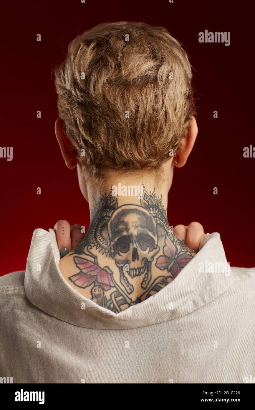 Vue arrière du tatouage du cou avec des mouettes et des papillons sur une jeune femme à poil court se posant sur fond rouge Banque D'Images