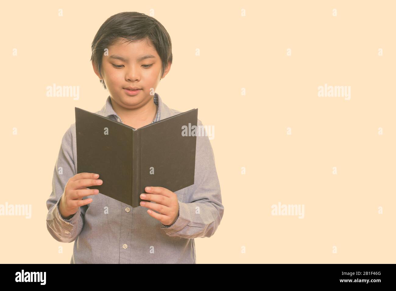 Studio shot of cute Japanese boy reading book Banque D'Images