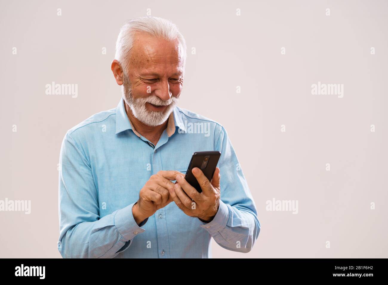 Portrait de l'homme senior gai qui utilise le smartphone. Banque D'Images