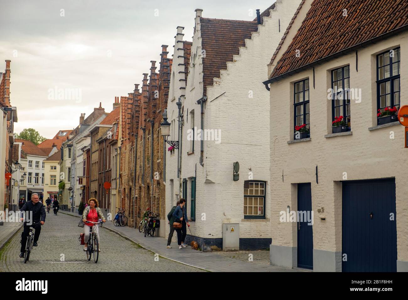 Deux personnes à vélo dans une rue pavée de Bruges.La rue est flanquée de maisons flamandes historiques. Banque D'Images Deux personnes à vélo dans une rue pavée de Bruges.La rue est flanquée de maisons flamandes historiques. Banque D'Images