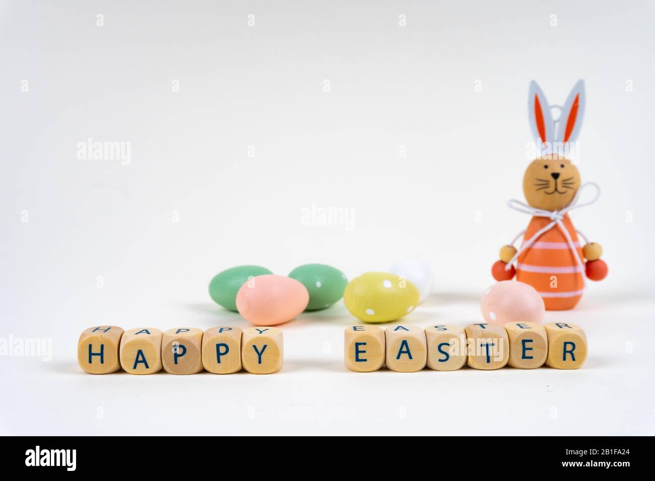 Blocs en bois avec des lettres disant "Joyeuses Pâques" devant des oeufs de pâques colorés et un lapin de pâques sur fond blanc avec espace de copie Banque D'Images