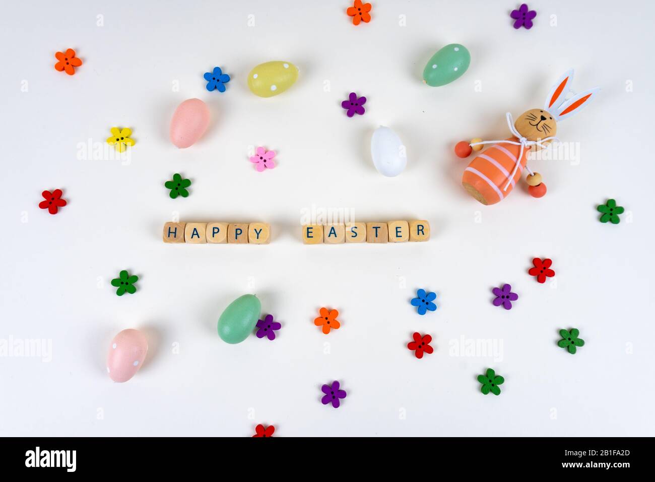 Blocs en bois avec des lettres disant "Joyeuses Pâques" devant des oeufs de pâques colorés, des fleurs colorées et un lapin de pâques sur fond blanc avec des copies Banque D'Images