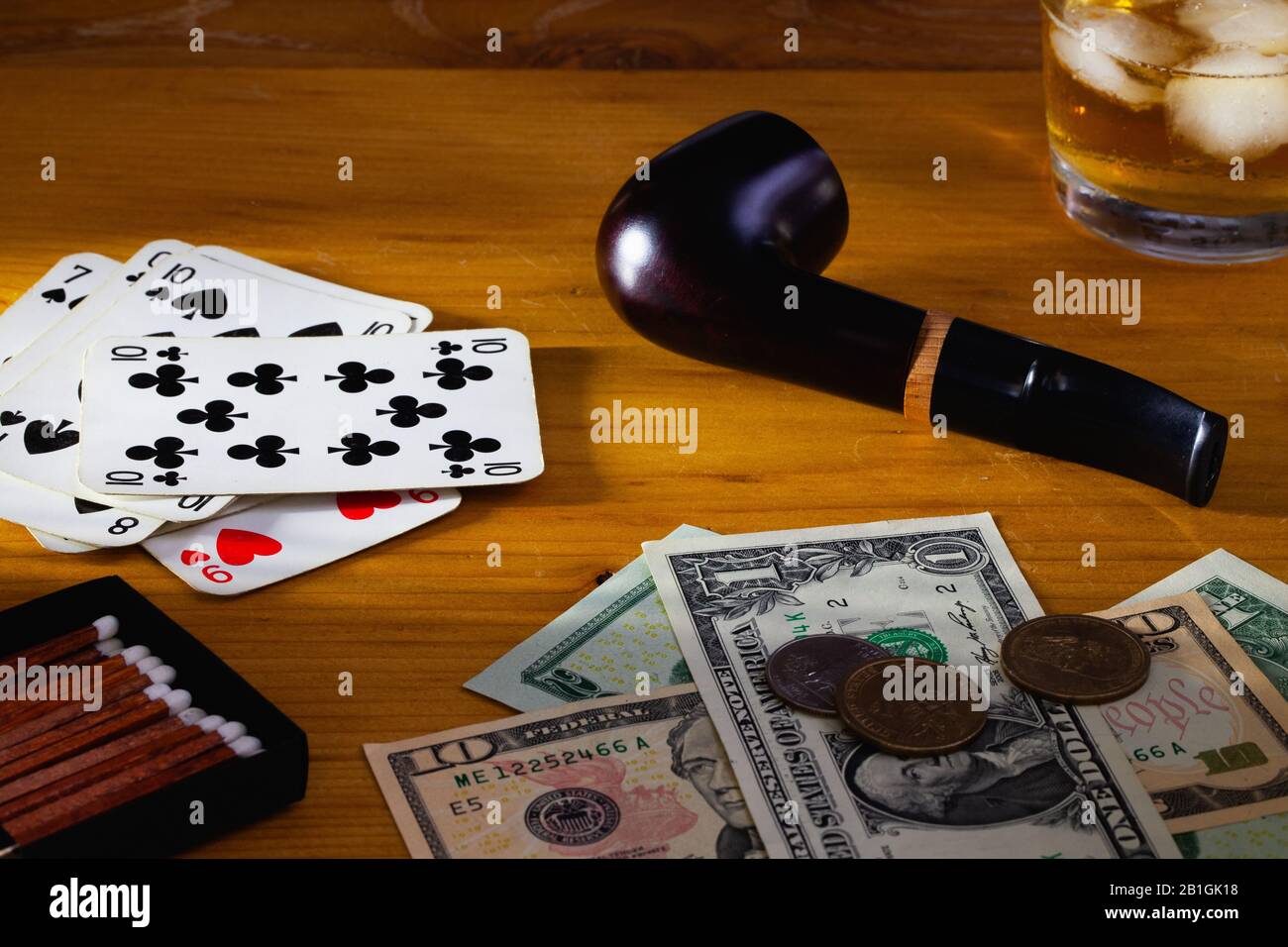 Jeux de hasard - tuyau de tabac , cartes à jouer, whisky écossais et billets en dollars américains sur la table en bois Banque D'Images
