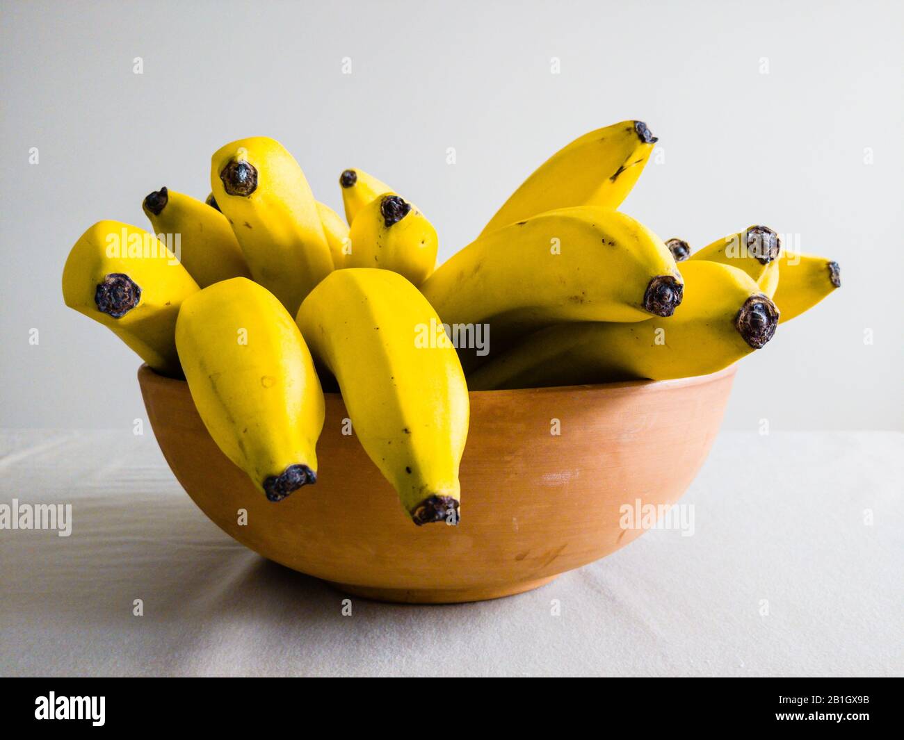 De nombreuses bananes jaunes dans un bol en céramique marron sur la table, vue de côté. Banque D'Images
