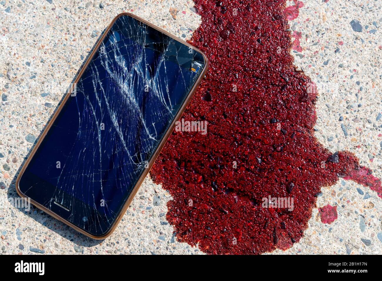 Un téléphone portable cassé et écrasé par une flaque de sang sur un trottoir. L'écran du téléphone portable est cassé et brisé. Le sang est frais. Banque D'Images