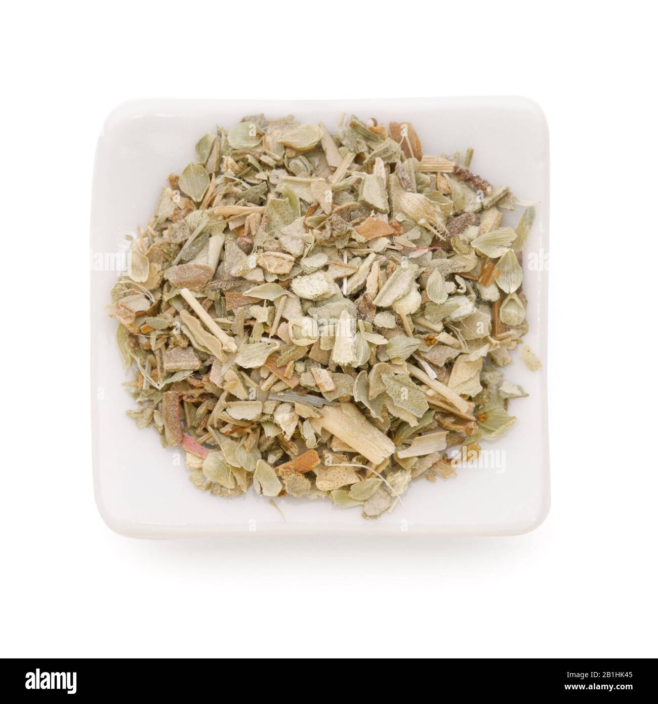 Basilic séché à la terre (basilic doux) dans un bol blanc sur fond blanc. Utilisé comme épice dans les herbes culinaires partout dans le monde. Banque D'Images