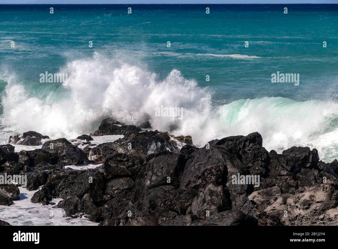 Rupture de la vague blanche contre les roches volcaniques noires sur la côte Kona de la Grande île d'Hawaï. Océan pacifique bleu-vert vif au loin. Banque D'Images