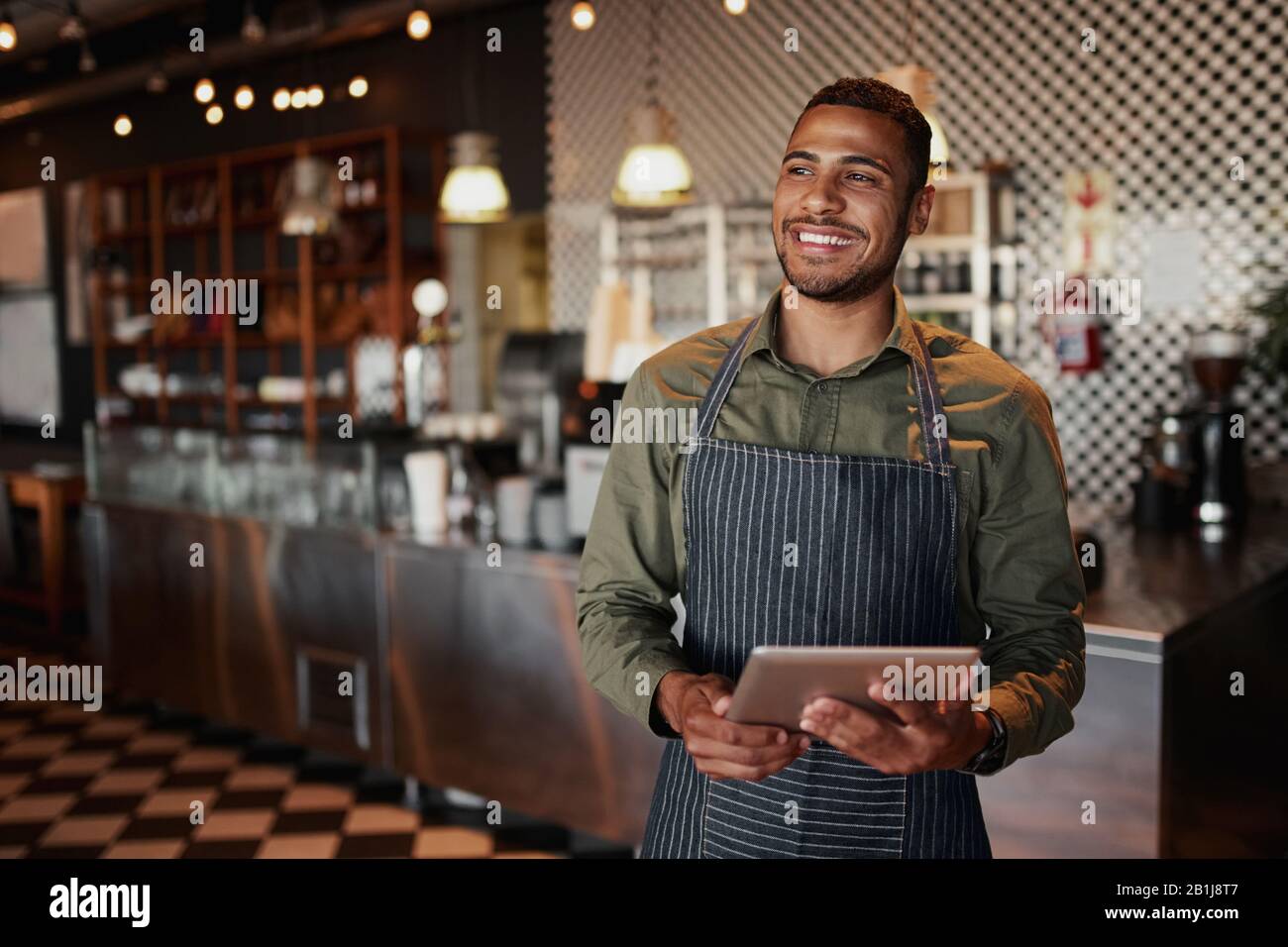 Jeune homme gai tenant une tablette numérique tout en se tenant dans un café Banque D'Images