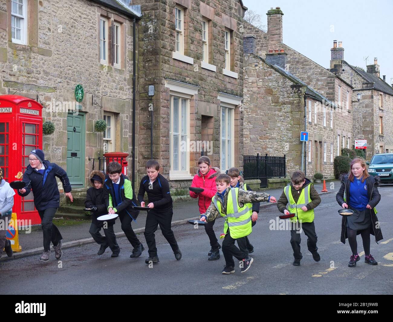 Les écoliers avec des poêles à frire et des crêpes au début d'une course pendant les Courses de pancake Winwer Shrove Mardi Pancake Day Derbyshire Royaume-Uni Banque D'Images