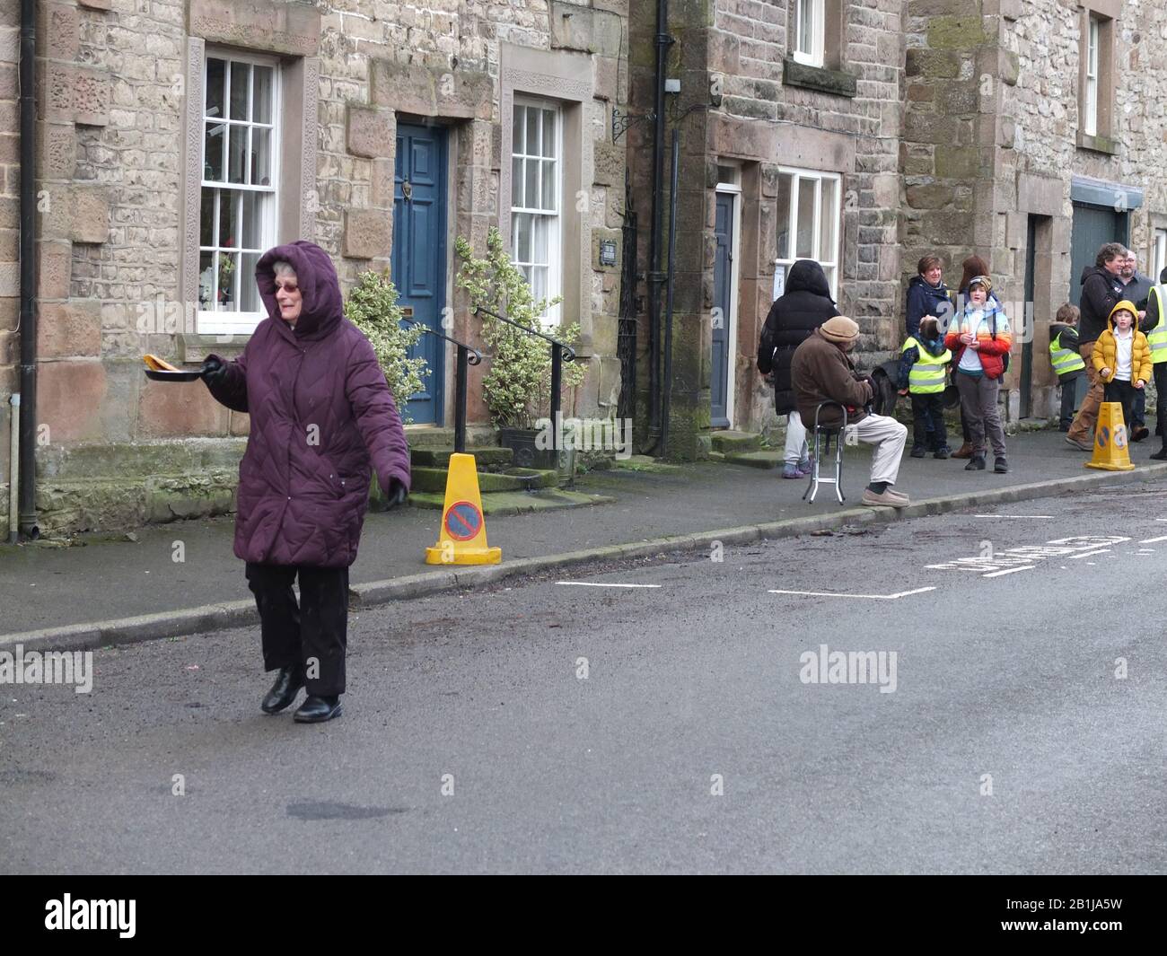 Concurrent dans la rue principale du village de Senior's Race Down avec poêle à frire et pancake pendant les Courses de pancake Winwer Shrove Mardi Pancake Day Derbyshire Banque D'Images