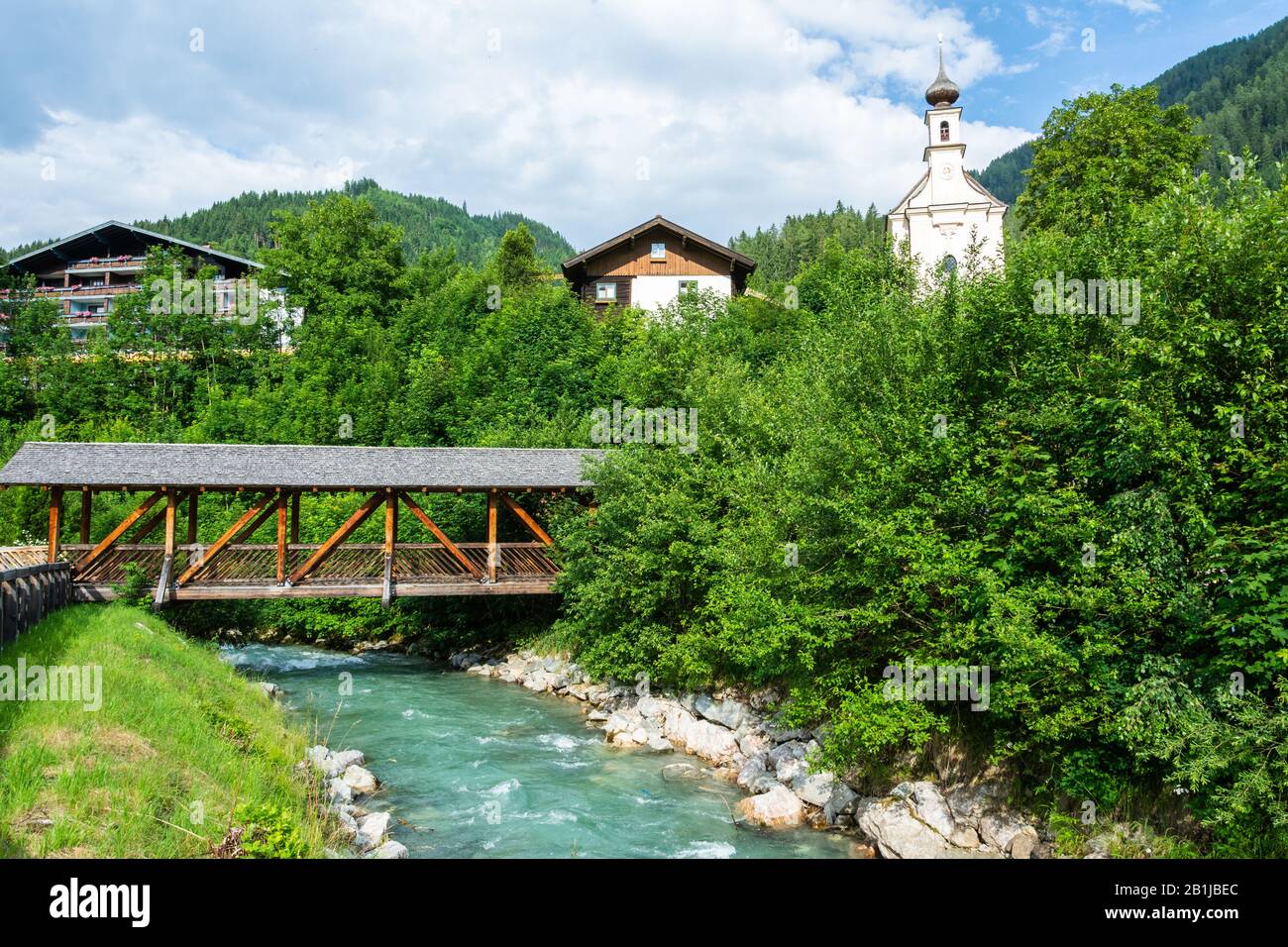 Vue sur la rivière Enns à Flachau, en Autriche, avec un pont couvert et une église paroissiale en arrière-plan. Banque D'Images