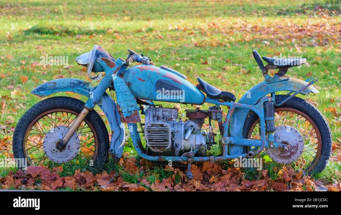 Vieille moto soviétique rouillée en bleu debout sur un fond d'herbe verte et de feuillage Banque D'Images