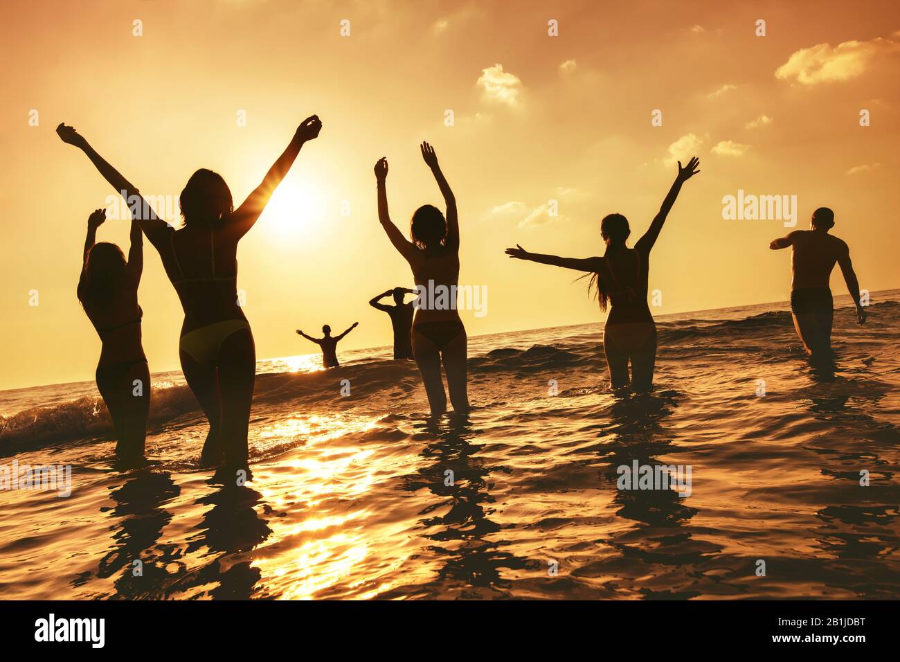 Un grand groupe de personnes heureux se tient à la plage de la mer au coucher du soleil. Silhouettes avec bras relevés Banque D'Images