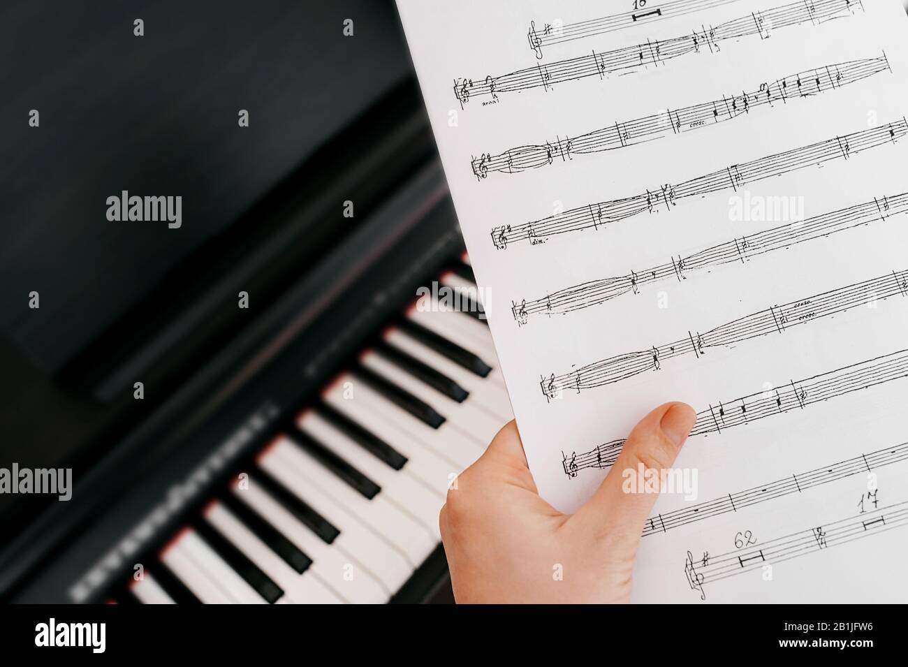 Une main tient des notes de musique sur le fond d'un synthétiseur de piano  électrique. Professeur de musique. Apprendre à jouer le piano Photo Stock -  Alamy