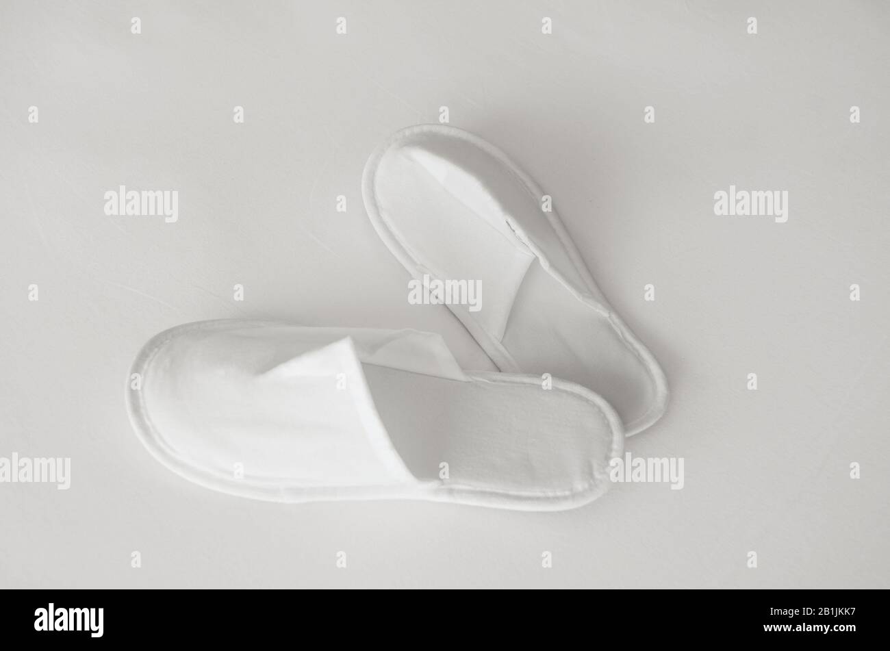 Les nouveaux chaussons jetables en tissu écologique fournis dans un emballage transparent se trouvent sur un drap blanc Banque D'Images