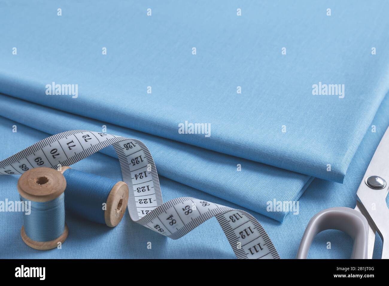 Jeu d'accessoires de personnalisation. Gros plan sur une pile de tissus bleus pliés, de ciseaux à coudre, de ruban de mesure blanc torsadé et de deux bobines de fil Banque D'Images