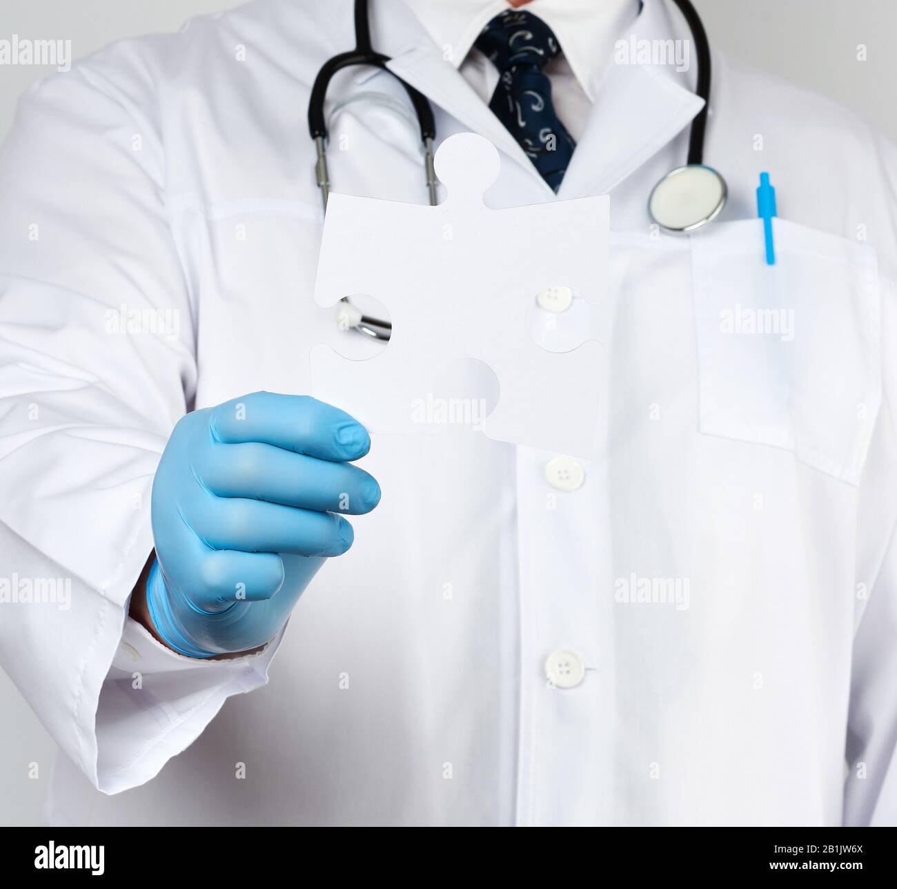 médecin dans un manteau médical blanc et des gants en caoutchouc bleu contient un puzzle en papier blanc, gros plan Banque D'Images