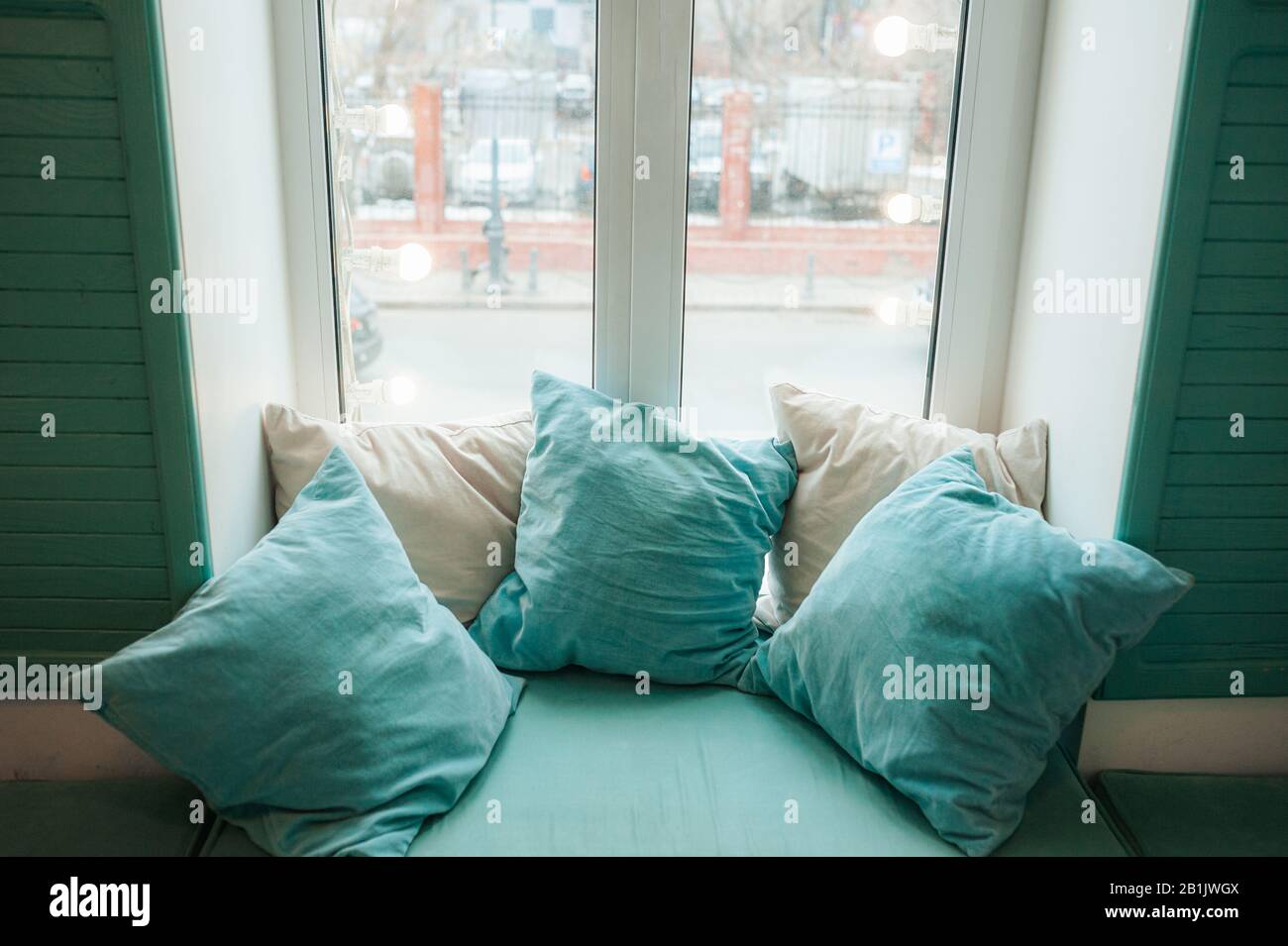 Un endroit doux et confortable près de la fenêtre avec des oreillers bleus et de couleur menthe. Un endroit pour se détendre et lire. Banque D'Images