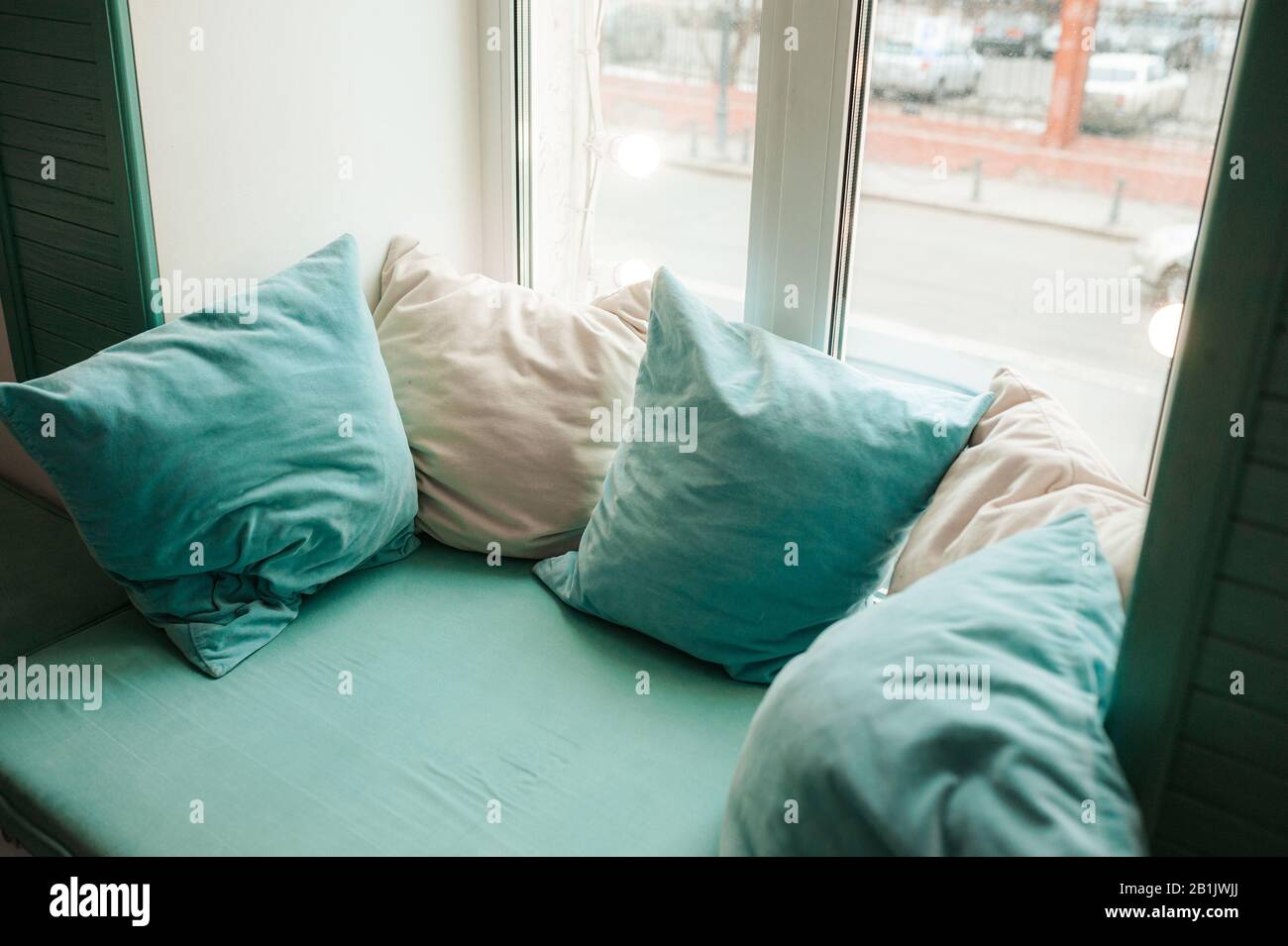 Un endroit doux et confortable près de la fenêtre avec des oreillers bleus et de couleur menthe. Un endroit pour se détendre et lire. Banque D'Images