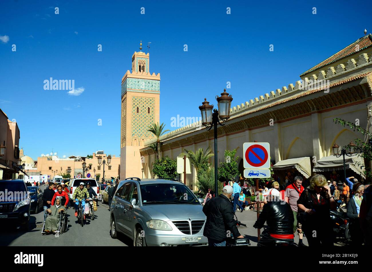 Marrakech, Maroc - 22 novembre 2014 : personnes non identifiées avec vélo, vélo et chaise non valide, mosquée avec minaret dans la structure traditionnelle Banque D'Images
