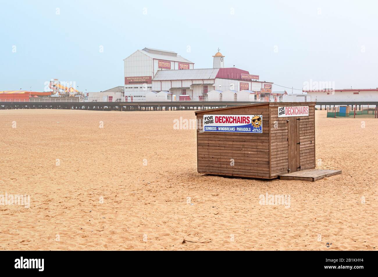 Un hangar en bois lapboard orné de deux panneaux peints de couleurs vives annonçant des chaises longues, etc. Se tient devant la brume enveloppée Britannia Pier Banque D'Images