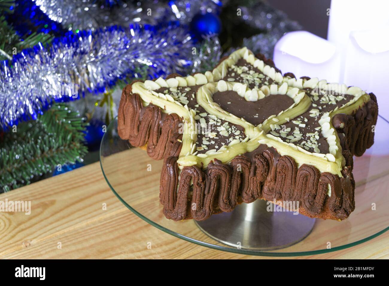 Gâteau fraîchement cuit en forme d'étoile avec un coeur à l'intérieur, décoré avec du chocolat naturel et des flocons d'amandes, sur un plateau en verre, sur une table en bois. Noël Banque D'Images