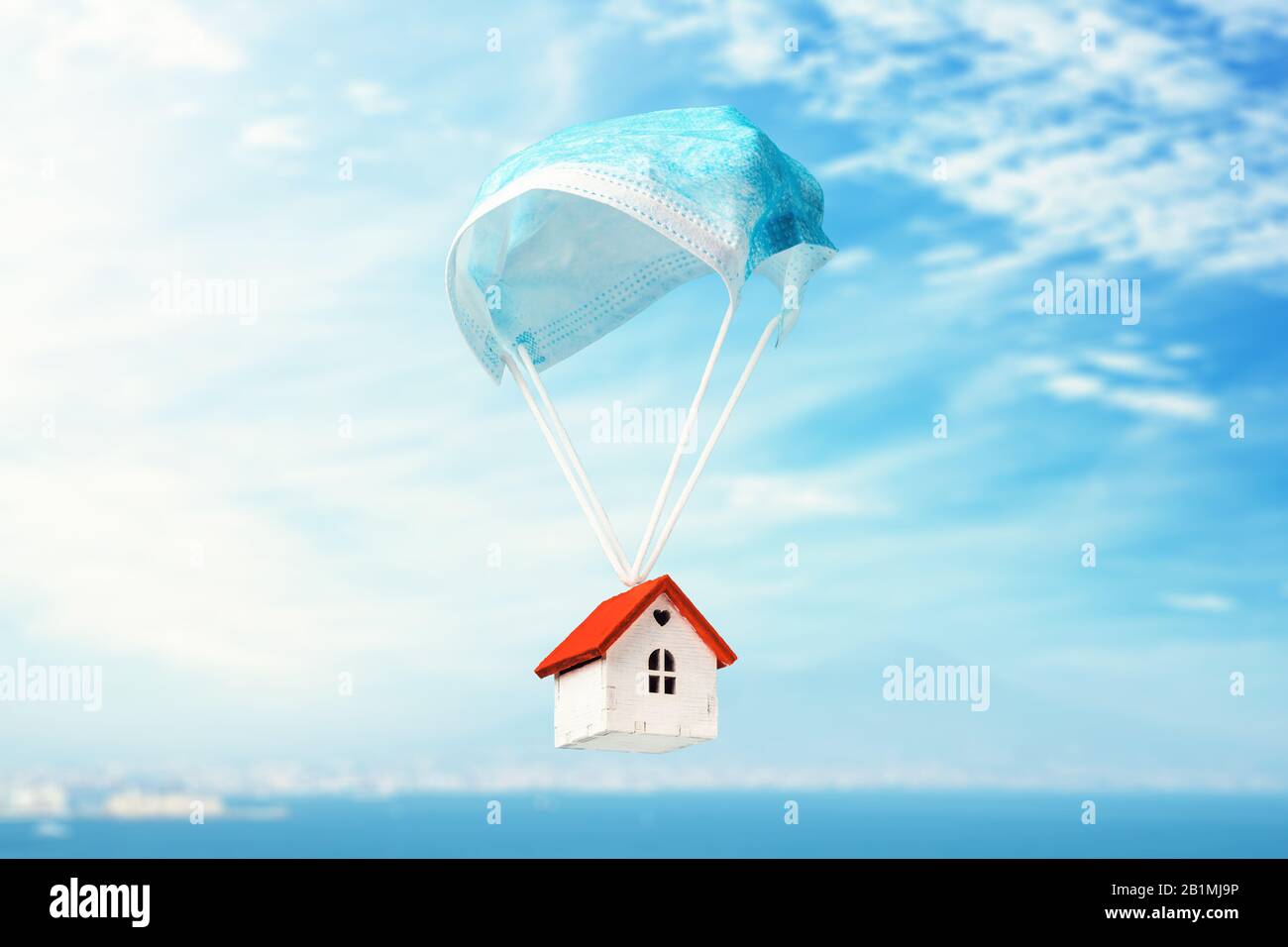 Une maison de jouets vole sur un parachute à partir d'un masque médical. Le concept d'une maison protégée contre les virus Banque D'Images