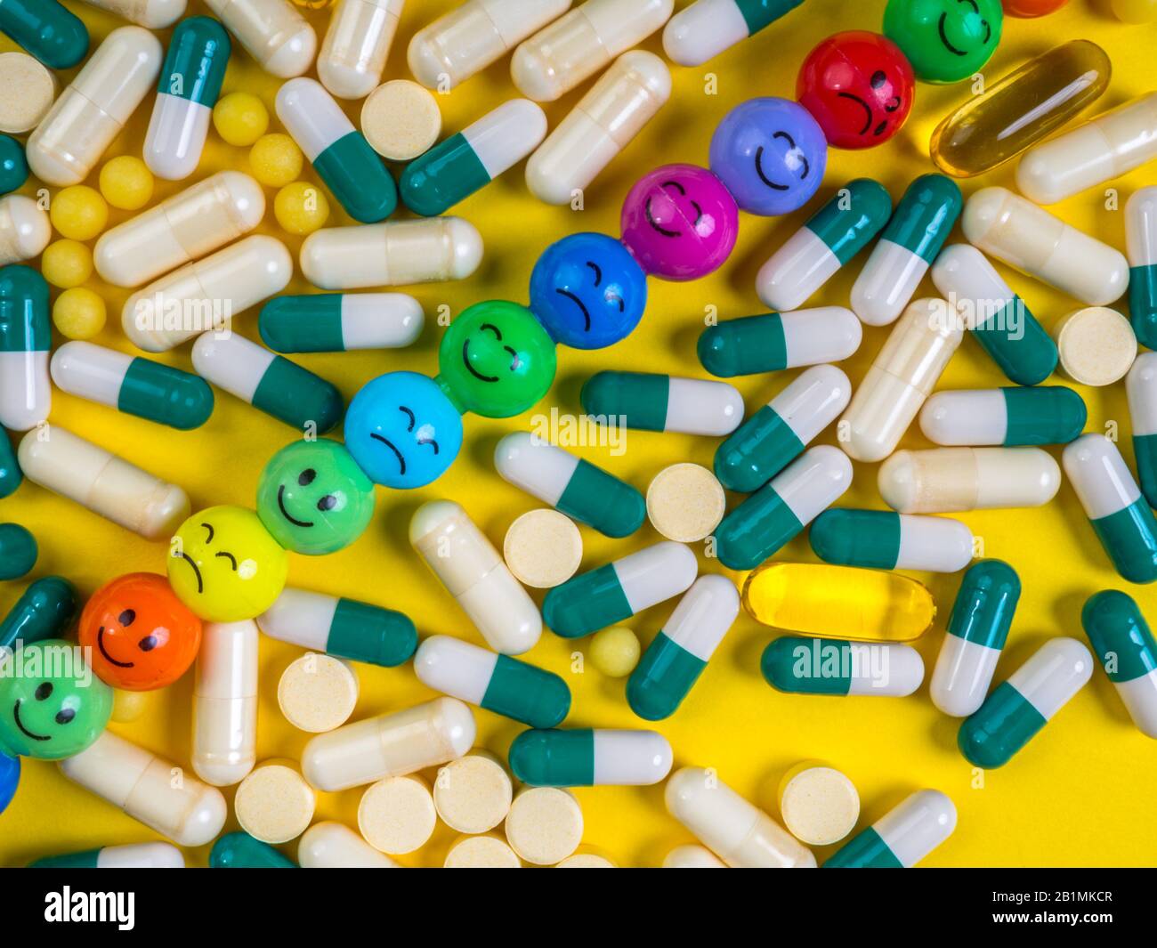 Pilules, comprimés et capsules multicolores avec des visages colorés et drôles d'émotions sur fond jaune. Concept de médecine. Guérison. Pilules antidépresseurs. Gros plan Banque D'Images