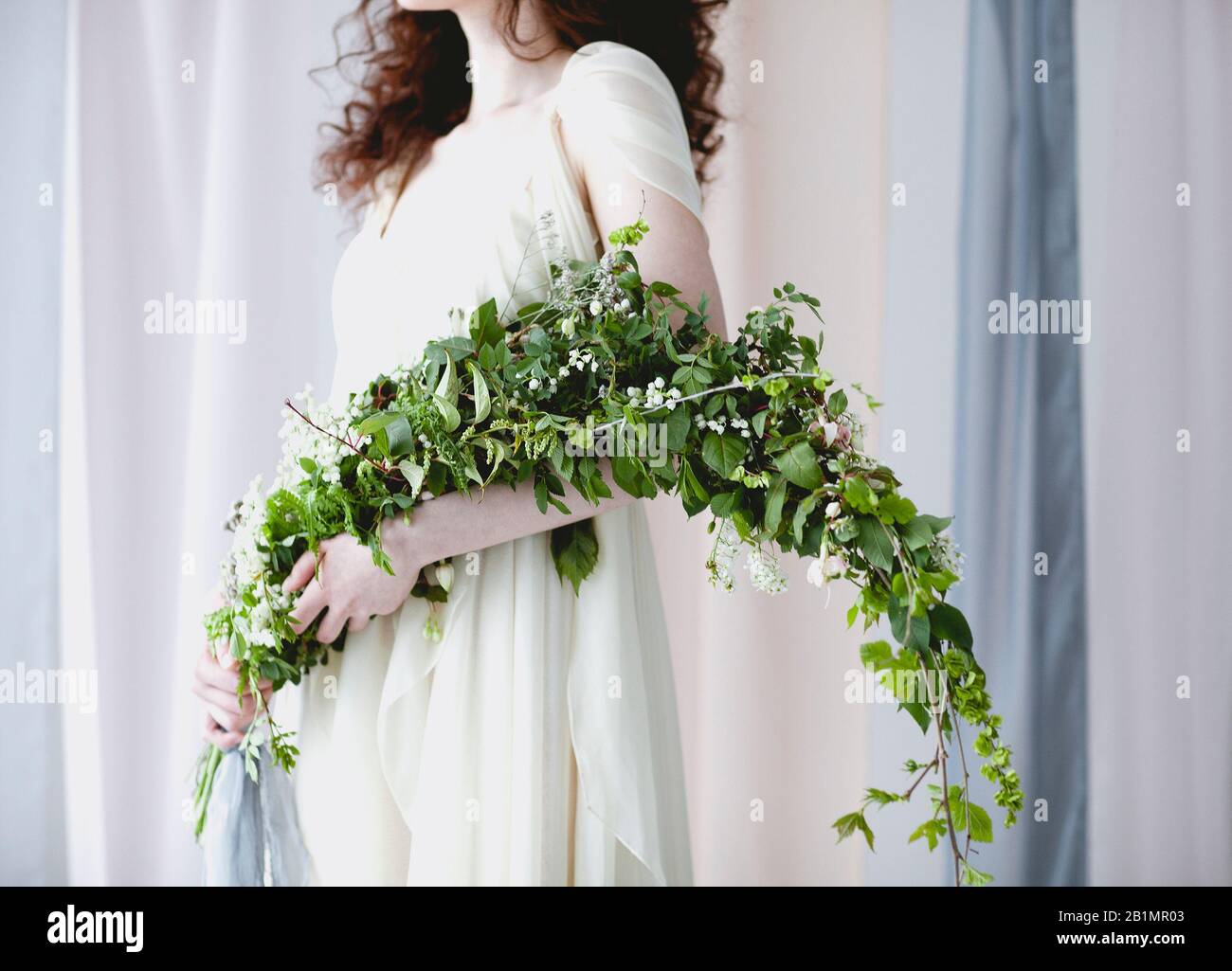 Chabillez une femme pieds nus dans une élégante robe de mariage blanche  avec un grand bouquet de petites fleurs blanches et un feuillage vert se  tenant dans une couleur pastel transparente c
