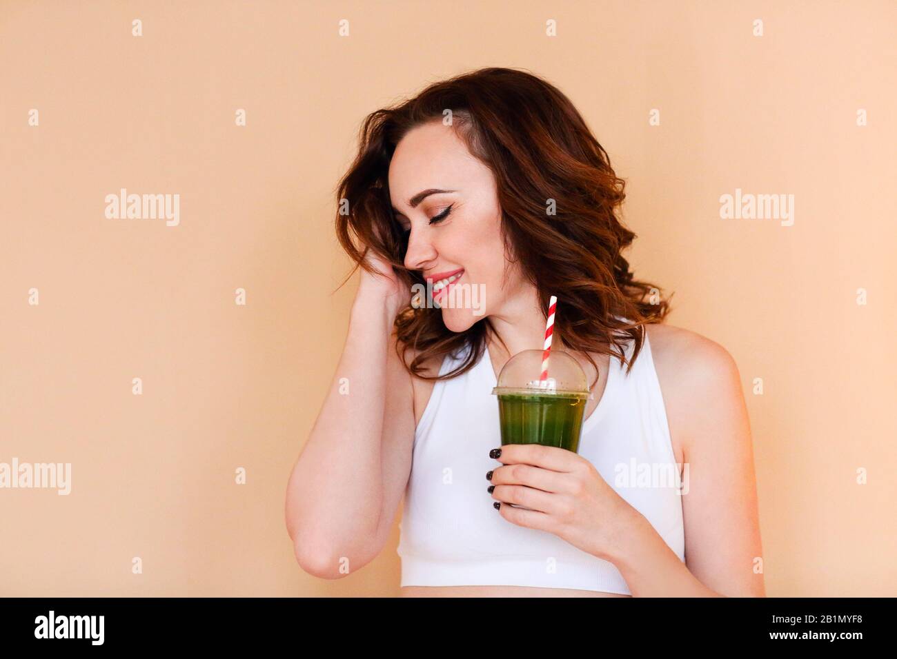 Crop a enchanté la jeune femme avec un smoothie vert riant contre le fond de mur Banque D'Images