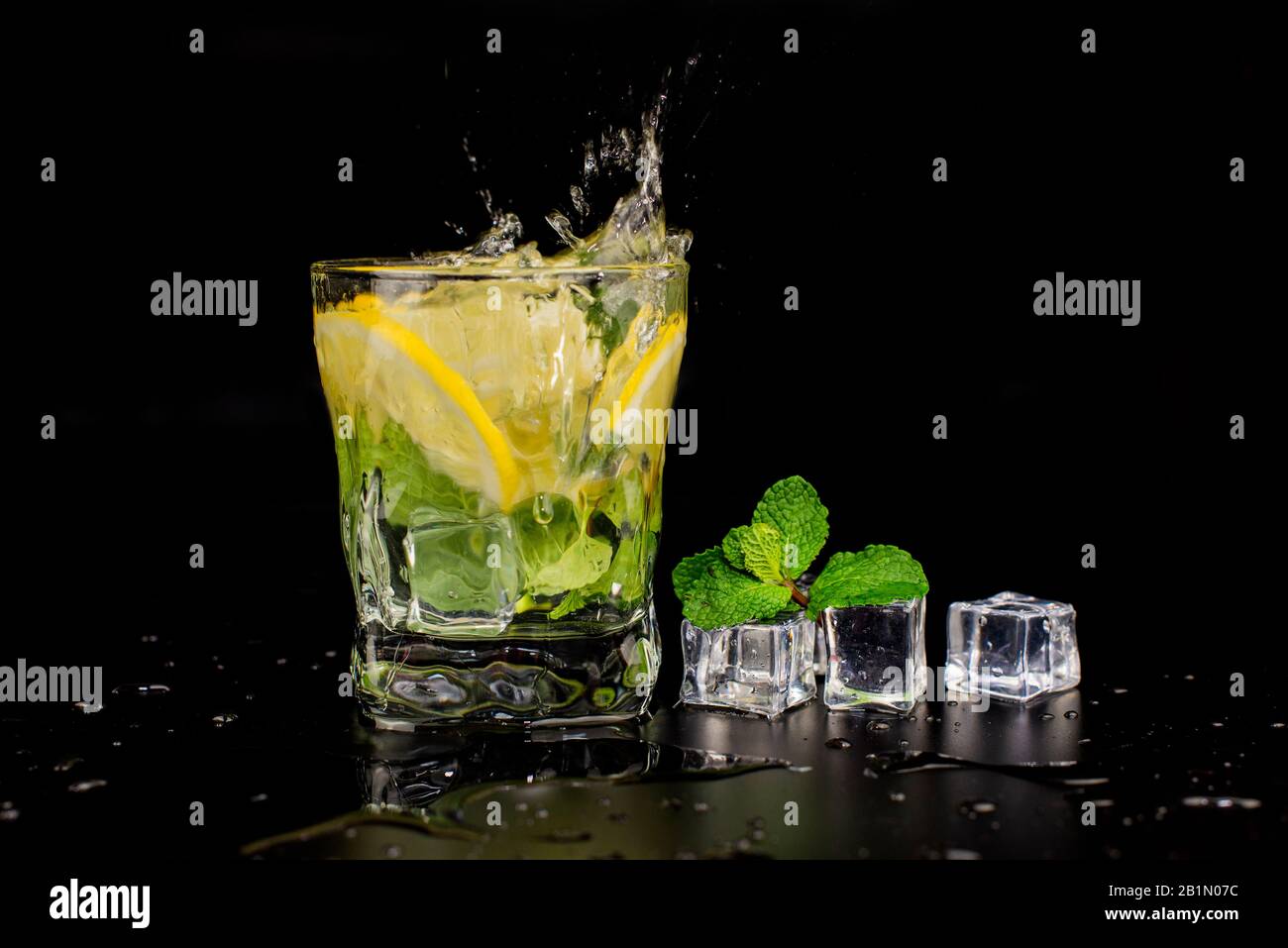 cocktail mojito avec menthe et citron vert dans un verre éclaboussant d'un verre avec glaçons, gouttes et éclaboussures sur fond noir Banque D'Images