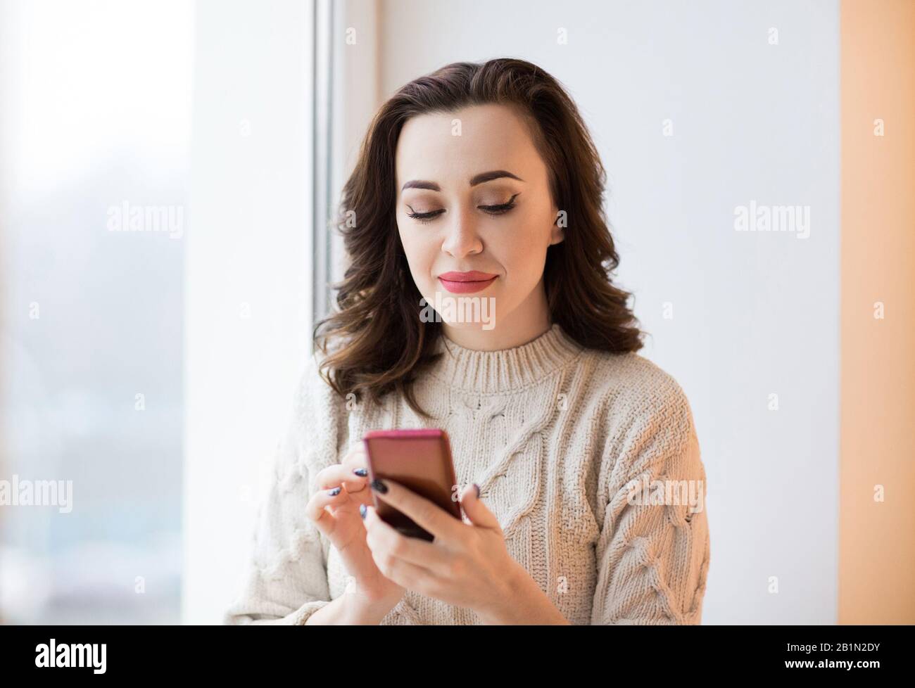 Femme dans un pull décontracté tricoté avec une manucure noire élégante à l'aide d'un téléphone mobile de vérification de message ou de navigation sur Internet Banque D'Images