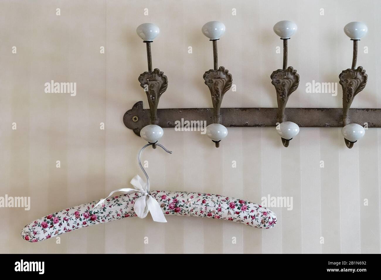 Élégant cintre en tissu fleuri recouvert de tissu suspendu sur un support mural brun vintage avec crochets blancs. Le cintre est décoré de ruban blanc. Banque D'Images