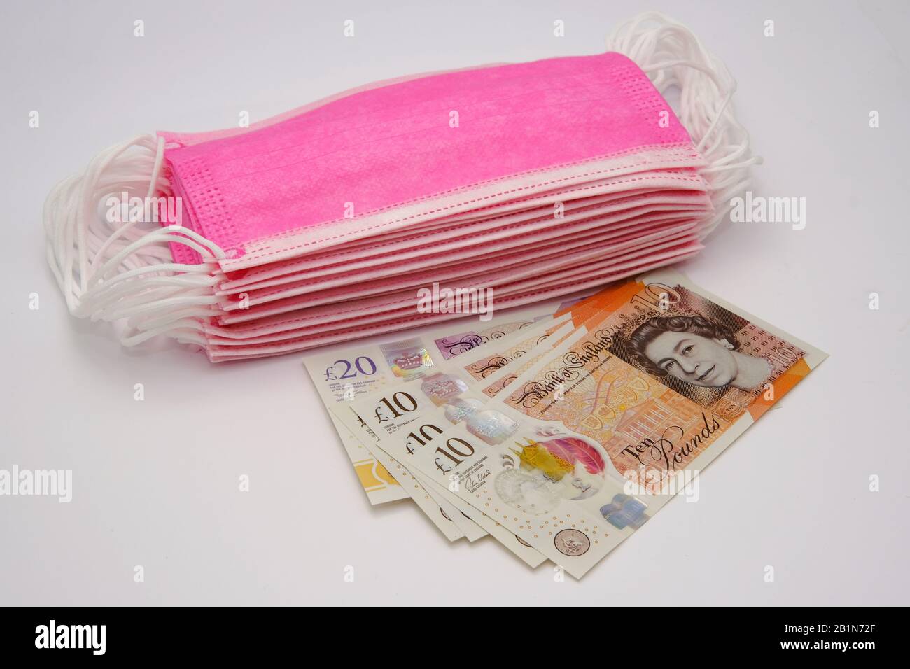 Masques roses pour la protection contre les virus et billet de billet de livre sterling. Concept de prix élevé des masques chirurgicaux pendant l'épidémie en Europe et au Royaume-Uni. Banque D'Images