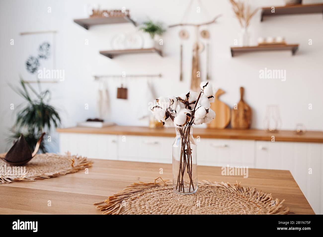 Un bouquet délicat de coton dans un petit vase transparent sur une serviette ronde en paille contre un intérieur de boho léger Banque D'Images